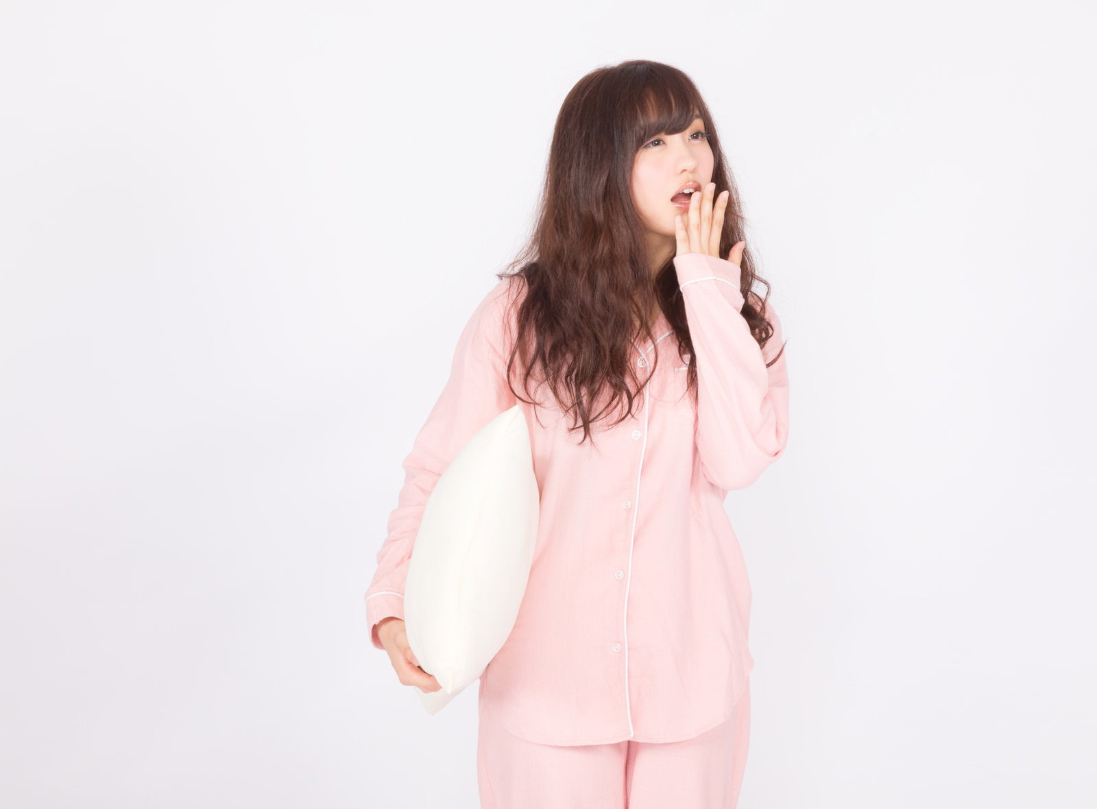 ピンクのパジャマを着た女性が手で口元を押さえながらあくびをしている［モデル：河村友歌］