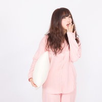 もう眠くて起きてられない...（あくび）ピンクのパジャマ姿の女性の写真