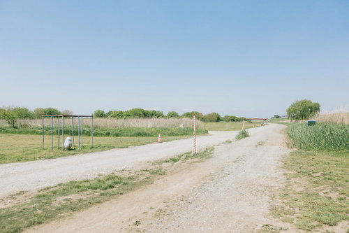 青空の下に広がる広い河川敷の草地と未舗装道路