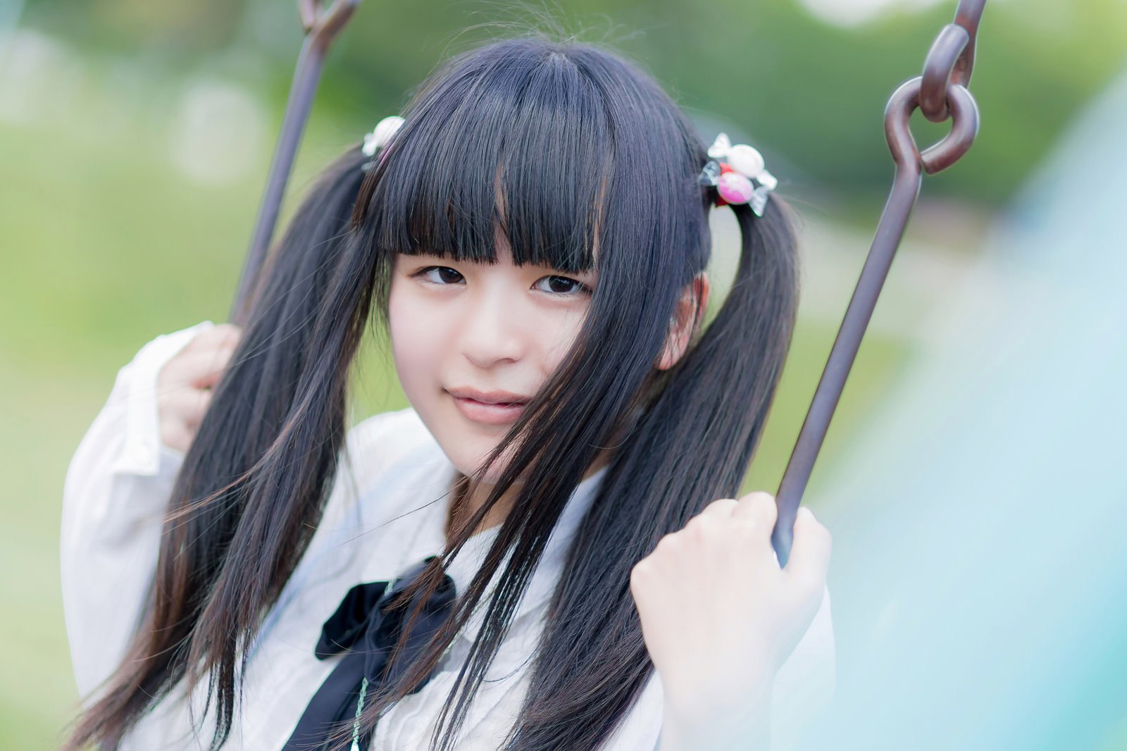 ブランコの鎖をつかむ花飾りのツインテールの女の子［モデル：こころ］