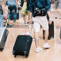 空港の混雑した通路でキャリーバッグを引く観光客たちの写真