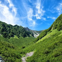 新緑溢れる山間から望む涸沢カールと青空、北アルプスの夏景色の写真