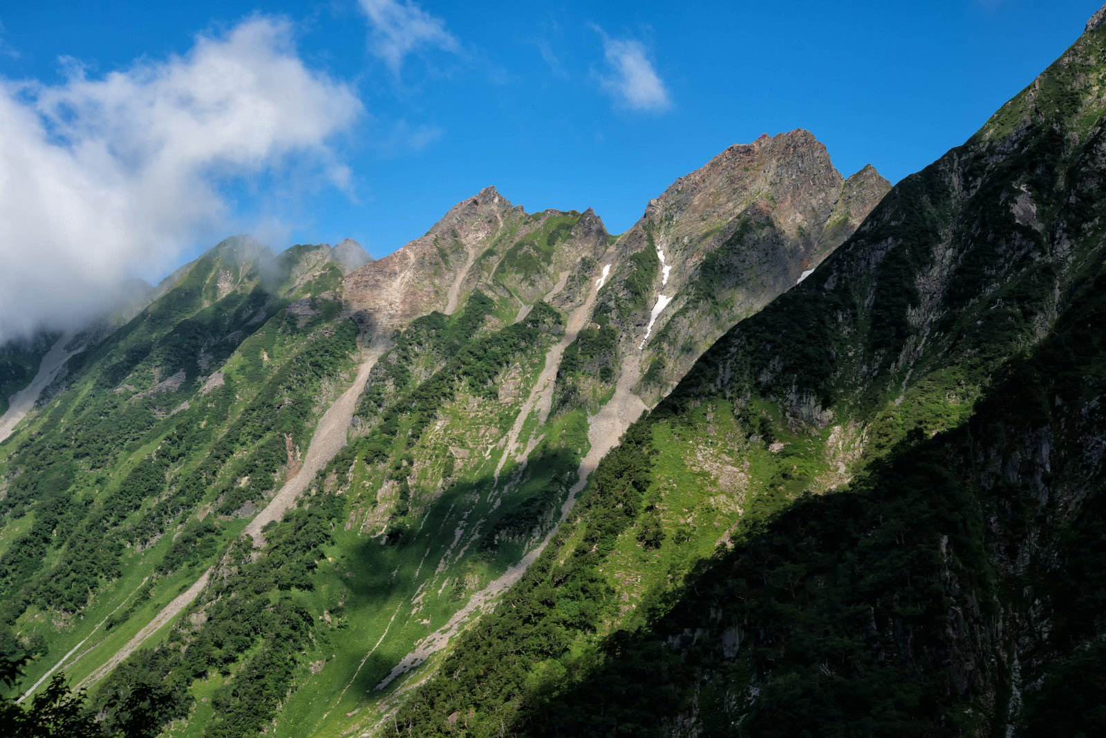 青空と雲に包まれた西穂高岳の険しい稜線と緑の山々