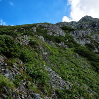 急峻な登山道に聳え立つ前穂高岳の岩肌と登山者の写真