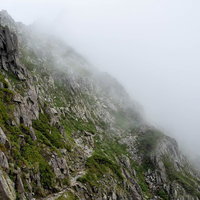 霧がたちこめる吊尾根の岩稜トラバース道を行く登山者の写真