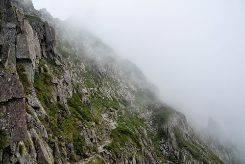 霧がたちこめる吊尾根の岩稜トラバース道を行く登山者