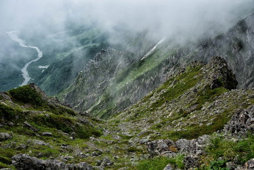 霧たちこめる吊尾根の岩壁稜線を行く登山道