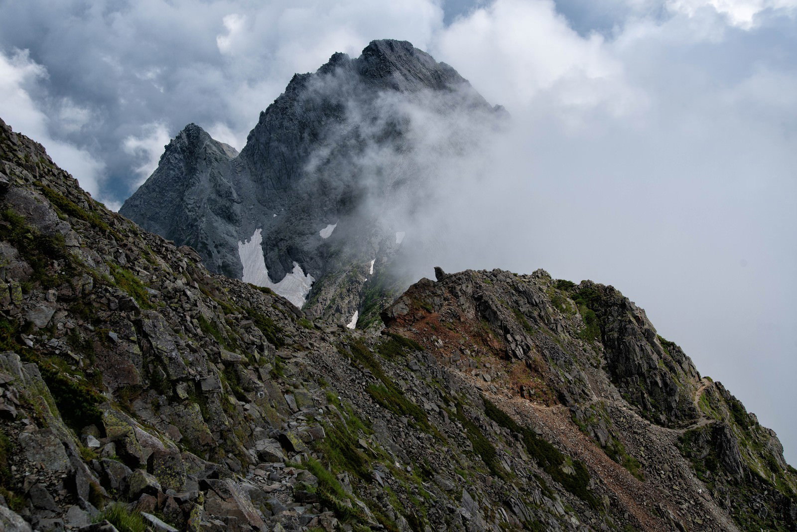 霧に包まれた険しい岩稜の登山道、雲が立ち上る山岳風景
