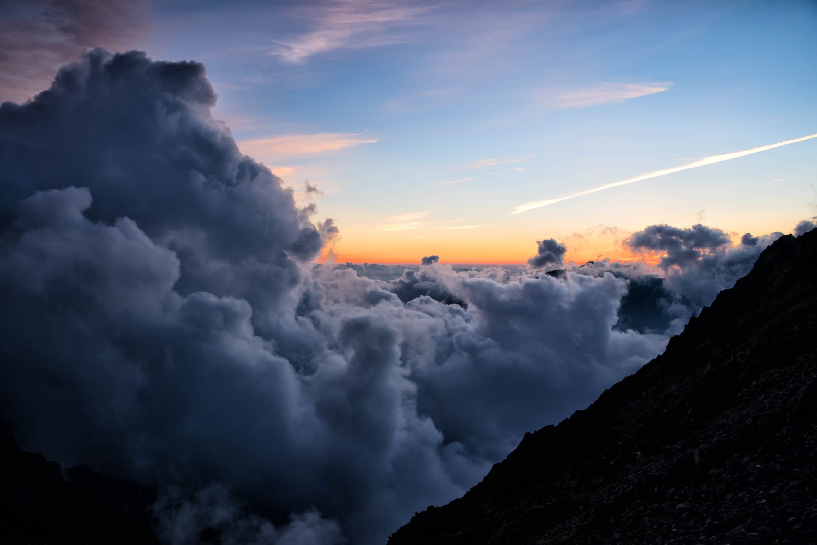 夕暮れ時に山の稜線から立ち上がる積雲が夕日に照らされている風景