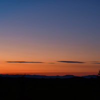 富良野の夕焼けに浮かぶ樹木のシルエットと雲の写真