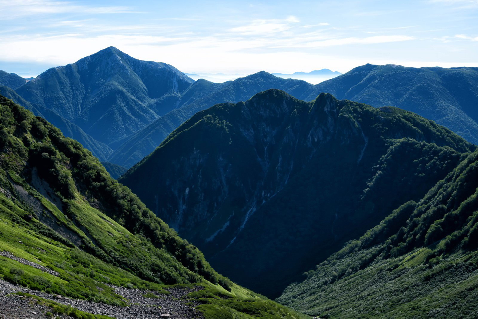 常念岳の深い谷間と緑の斜面、背景に連なる山々