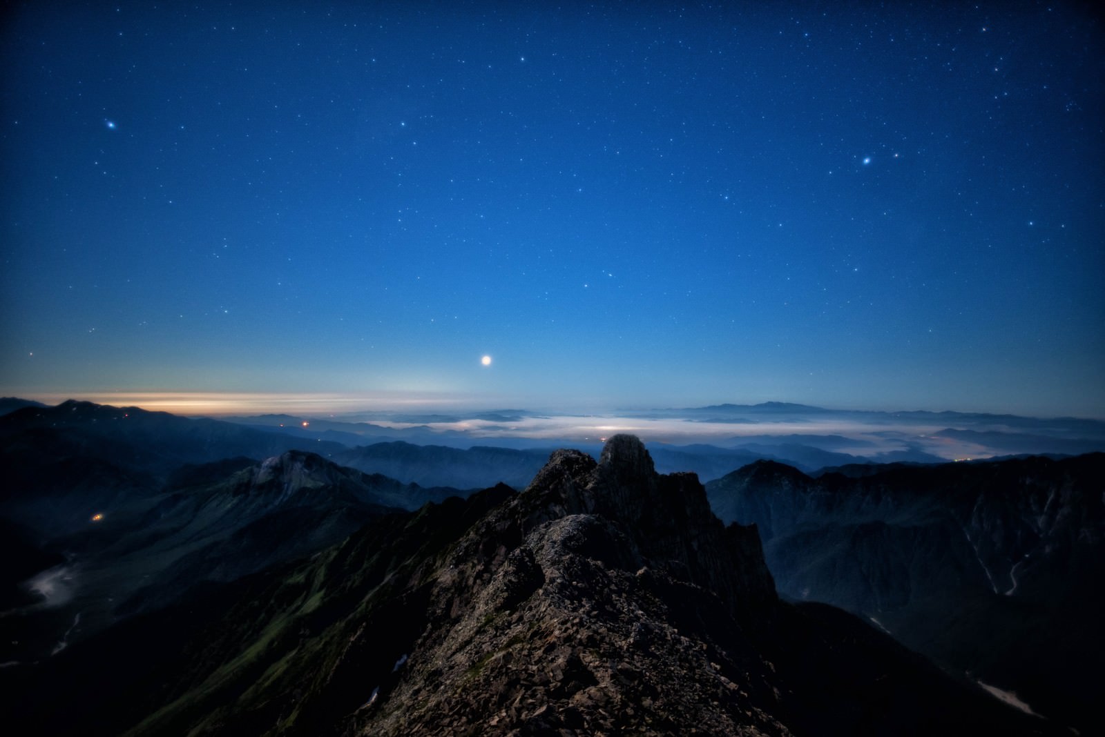 深い青色の夜空に星が輝き、眼下に雲海が広がるジャンダルムの山峰