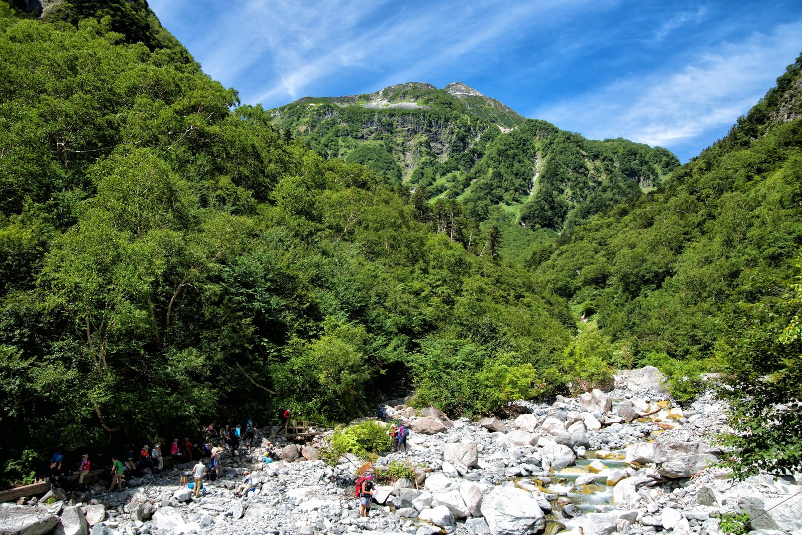 本谷橋の渓谷で水場に集まり休憩する登山者たちと緑の森