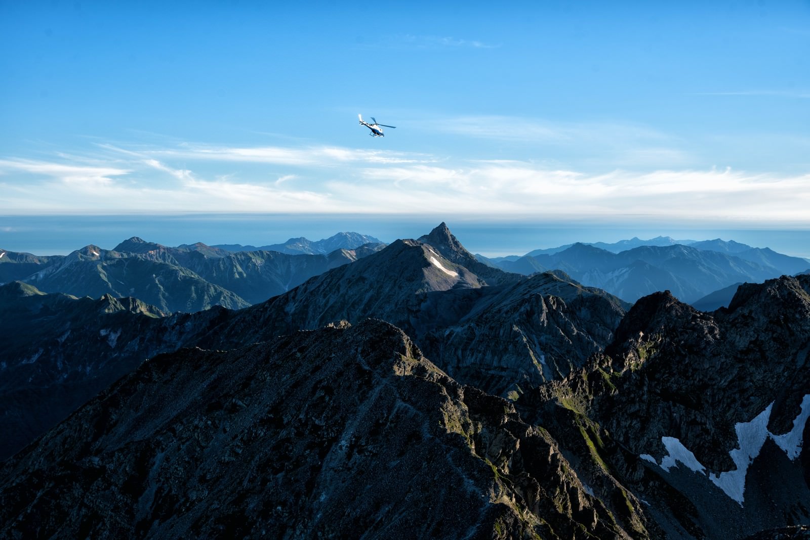 青空の下、槍ヶ岳方面の山岳地帯上空を飛行するヘリコプター