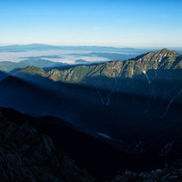 穂高から伸びる影と笠ヶ岳の尾根を望む山岳風景の写真