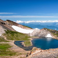 雪解けの水が溜まる権現池と登山道の残雪が見える春の山風景の写真