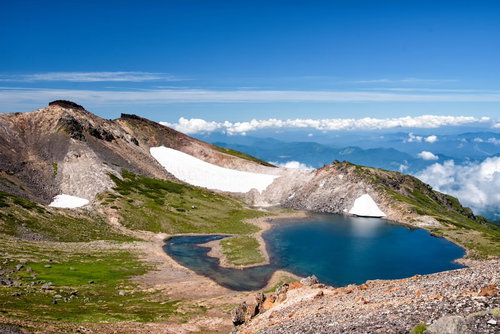 雪解けの水が溜まる権現池と登山道の残雪が見える春の山風景