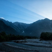 夜明けの上高地を流れる川と山峰、朝焼けに染まる渓谷の風景の写真