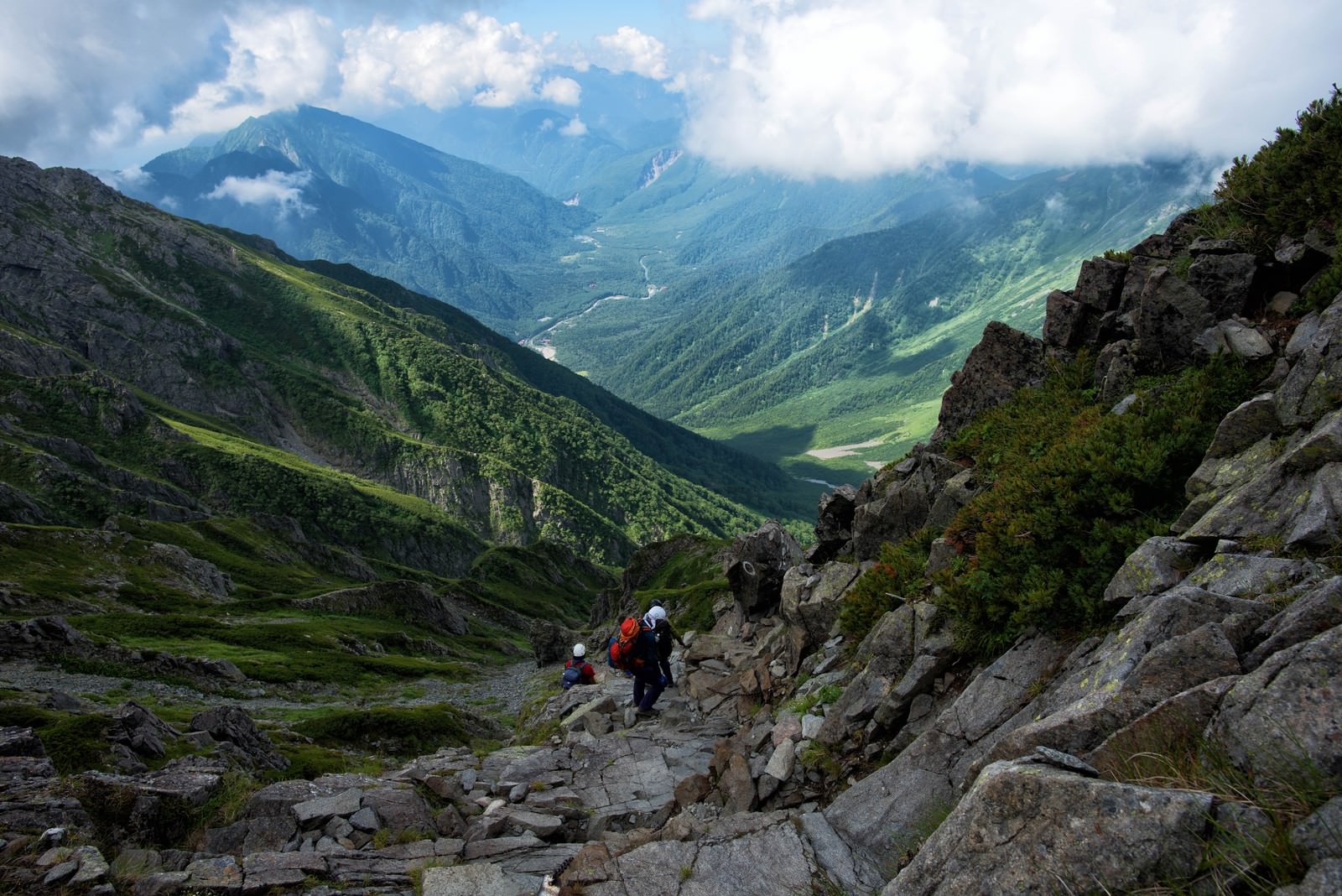 険しいガレ場の登山道を歩く登山者と山岳風景