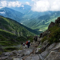 ガレ場に挑む登山者と青空の山岳風景の写真