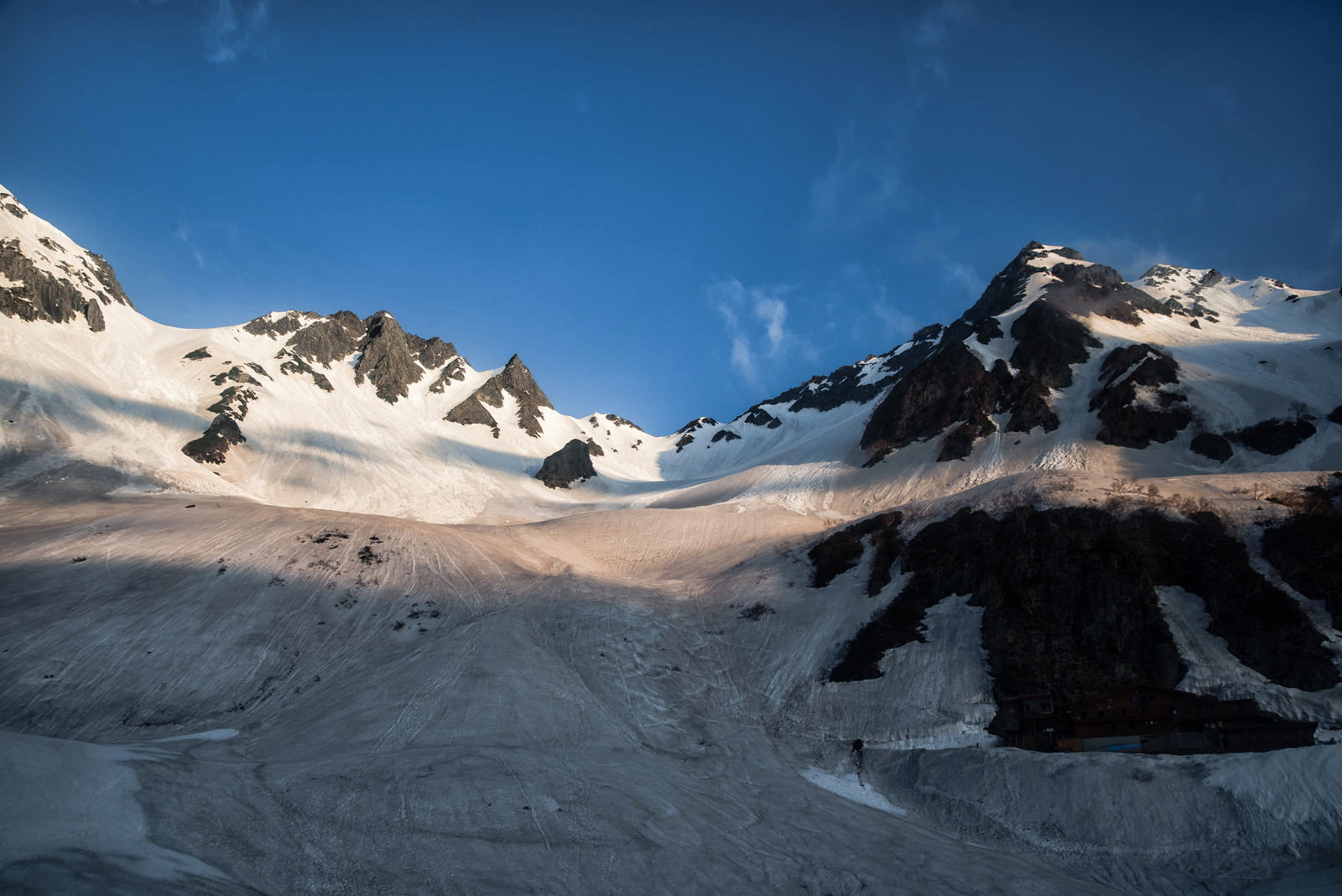 青空の下、雪に覆われた涸沢の山々と山小屋の影が雪面に落ちている冬山の風景