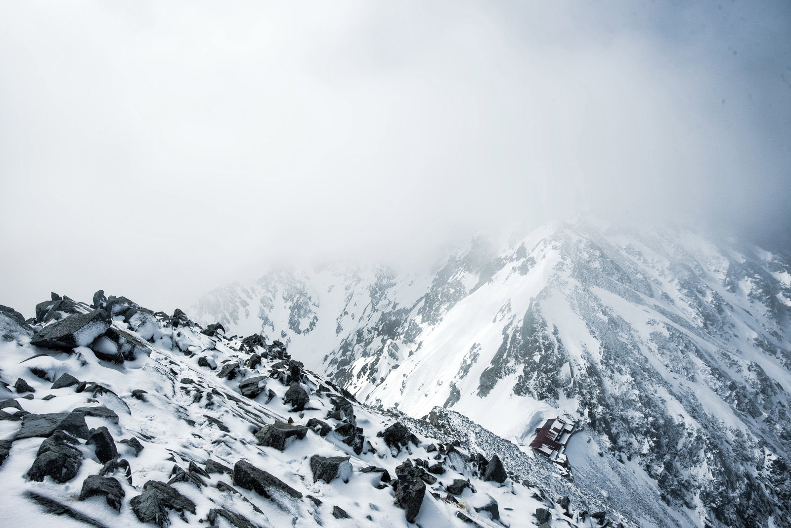 雪化粧した穂高連峰の稜線が霧とガスに覆われている冬山の風景
