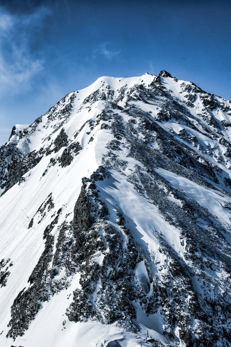 雪に覆われた奥穂高岳の険しい岩肌と登山道、青空と雲