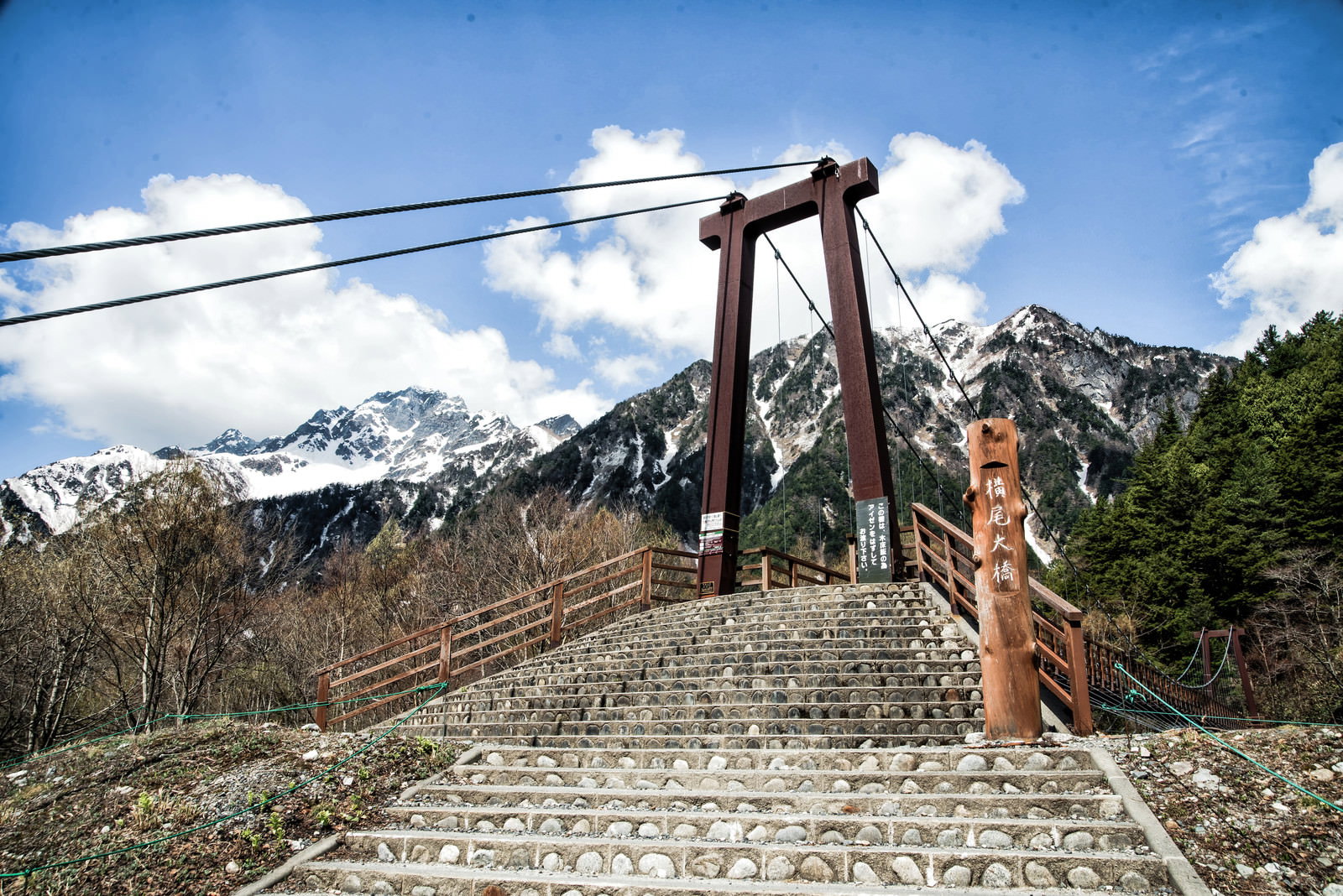 木製の吊り橋の階段から見た雪化粧した明神岳の山々と青空