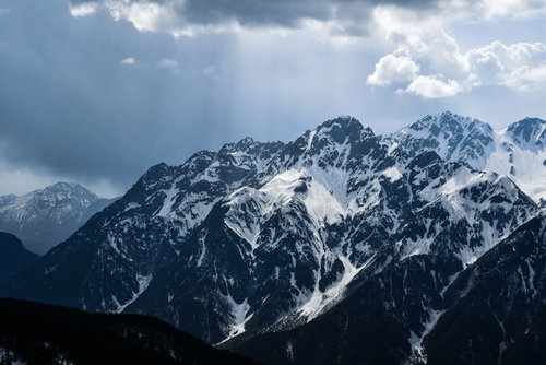 雲間からの光に照らされる雪化粧の前穂高岳（北アルプス）