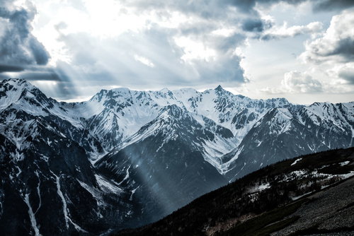 雲間から差し込む光芒と雪化粧の槍ヶ岳、飛騨山脈の冬景色