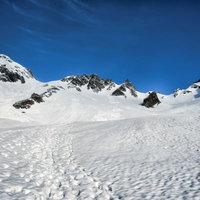 残雪期の涸沢岳の雪山に続く登山者の足跡が点々と連なる風景の写真