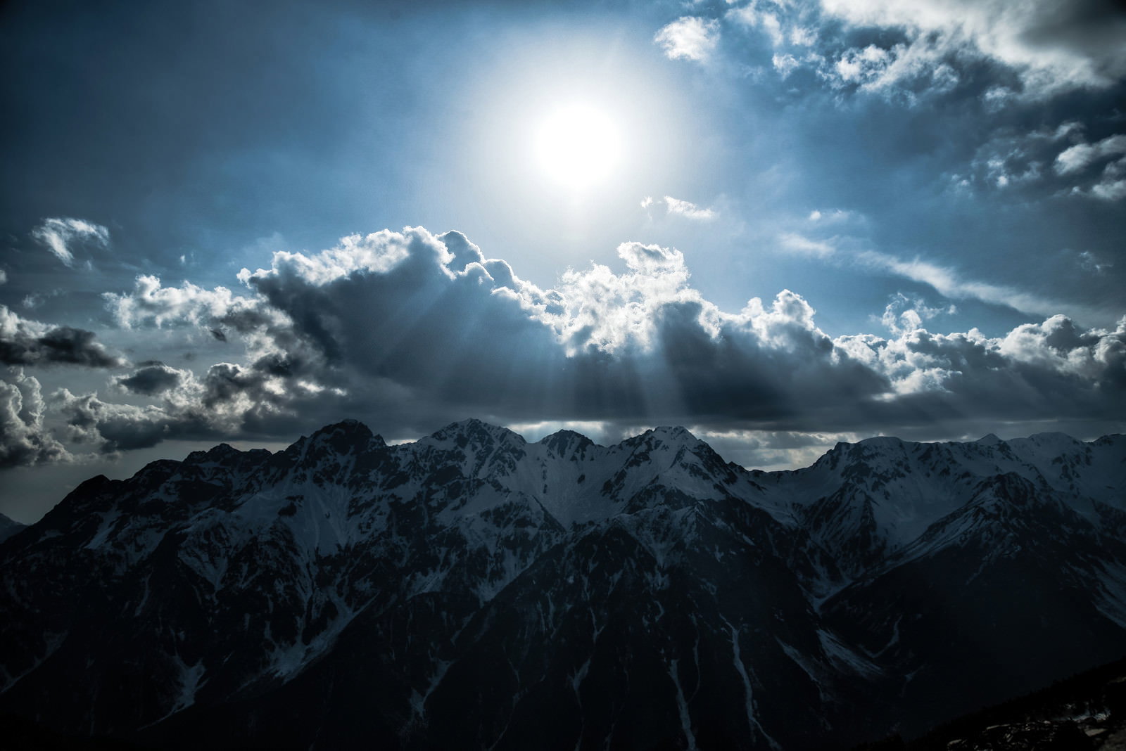 雲間から差し込む天使のはしごが残雪の飛騨山脈を照らす光景