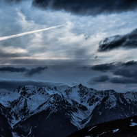 冬山の槍ヶ岳上空を横切る飛行機雲と積雪の山頂の写真