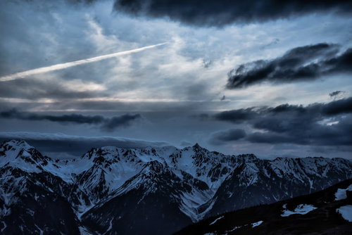 冬山の槍ヶ岳上空を横切る飛行機雲と積雪の山頂