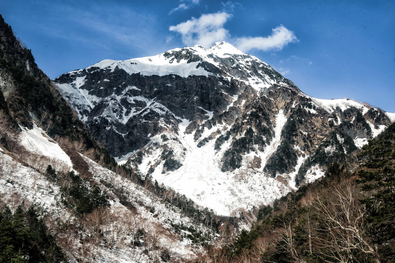 青空の下、雪に覆われた北穂高岳の岩壁がそびえ立つ北アルプスの山岳風景