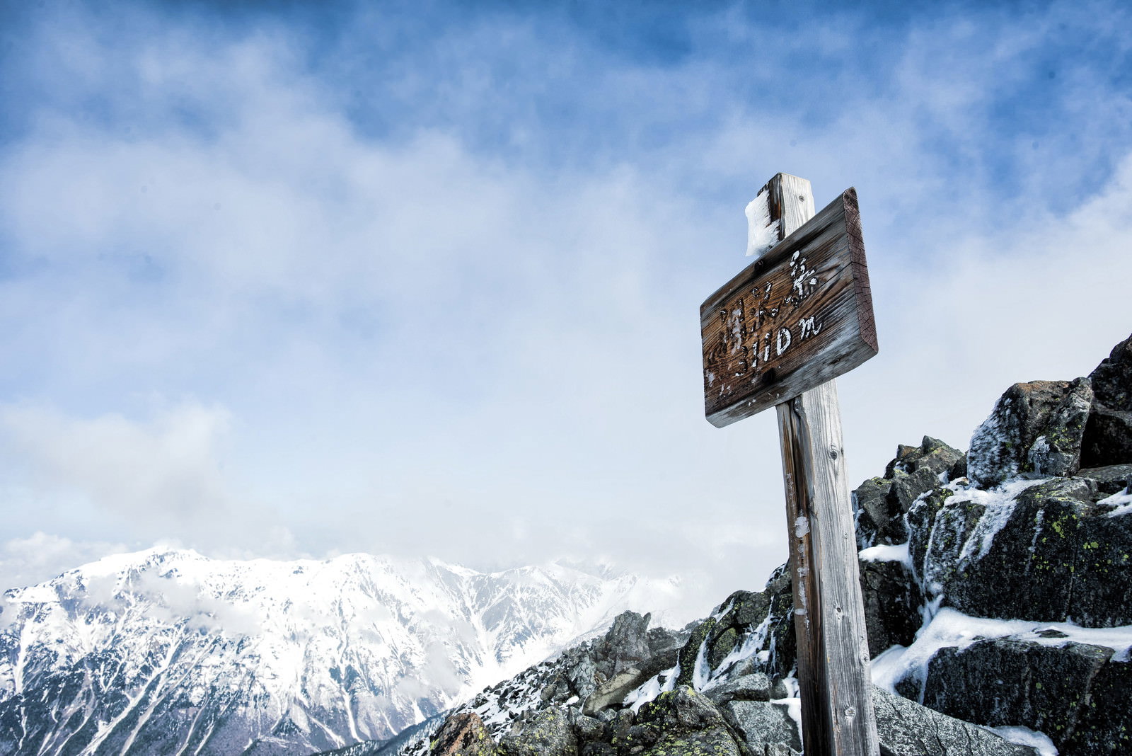 雪山の山頂に立つ涸沢岳の山頂標と青空に浮かぶ雲