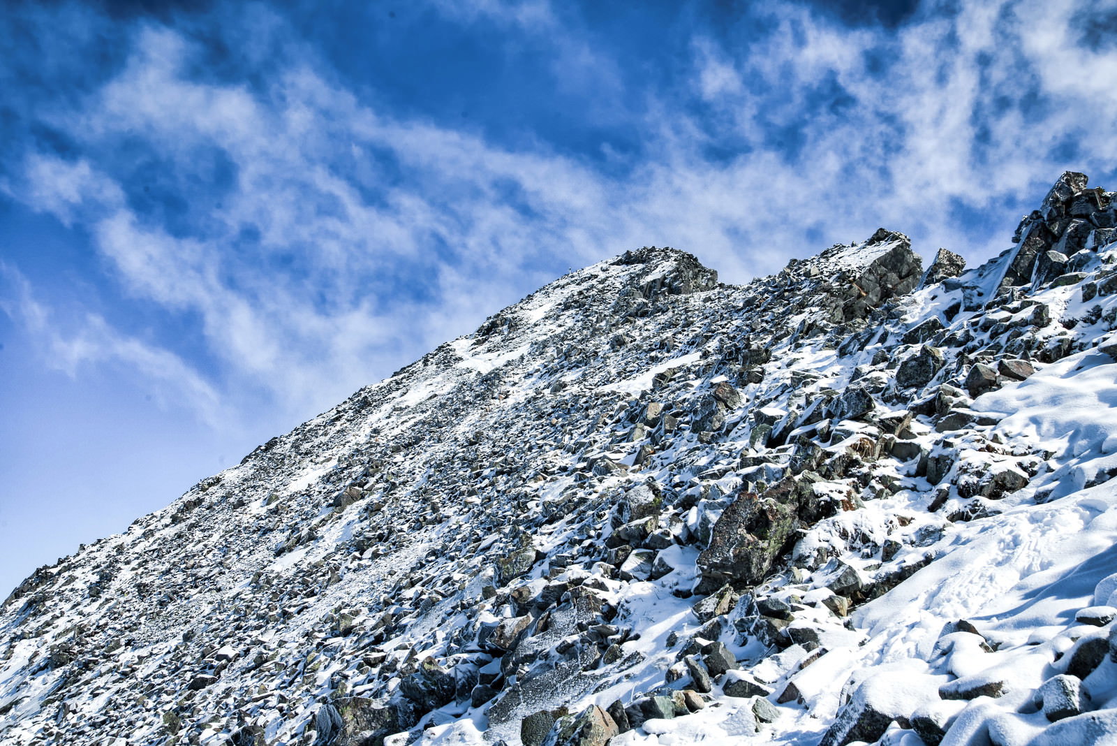 青空の下、雪に覆われた涸沢岳の急峻な岩肌と登山道