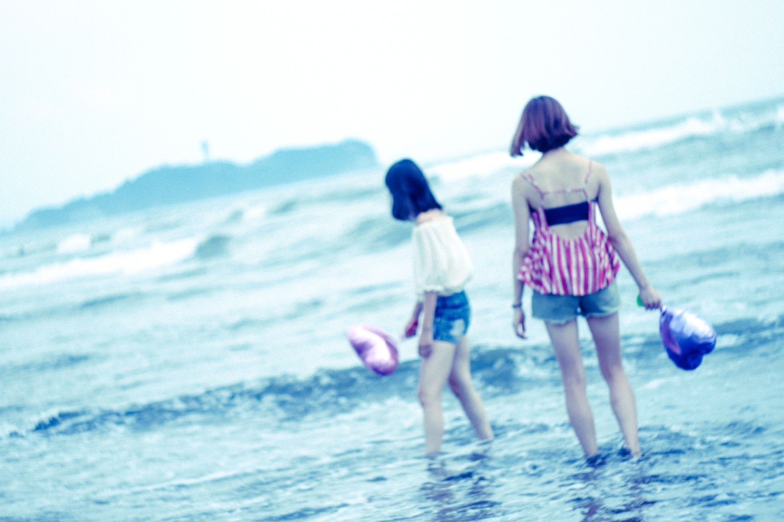 夏の海で波打ち際を歩く2人の女性の後ろ姿をソフトフォーカスで撮影した写真