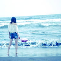 波打ち際で浅瀬の波と戯れる白いワンピース姿の若い女性の後ろ姿の写真