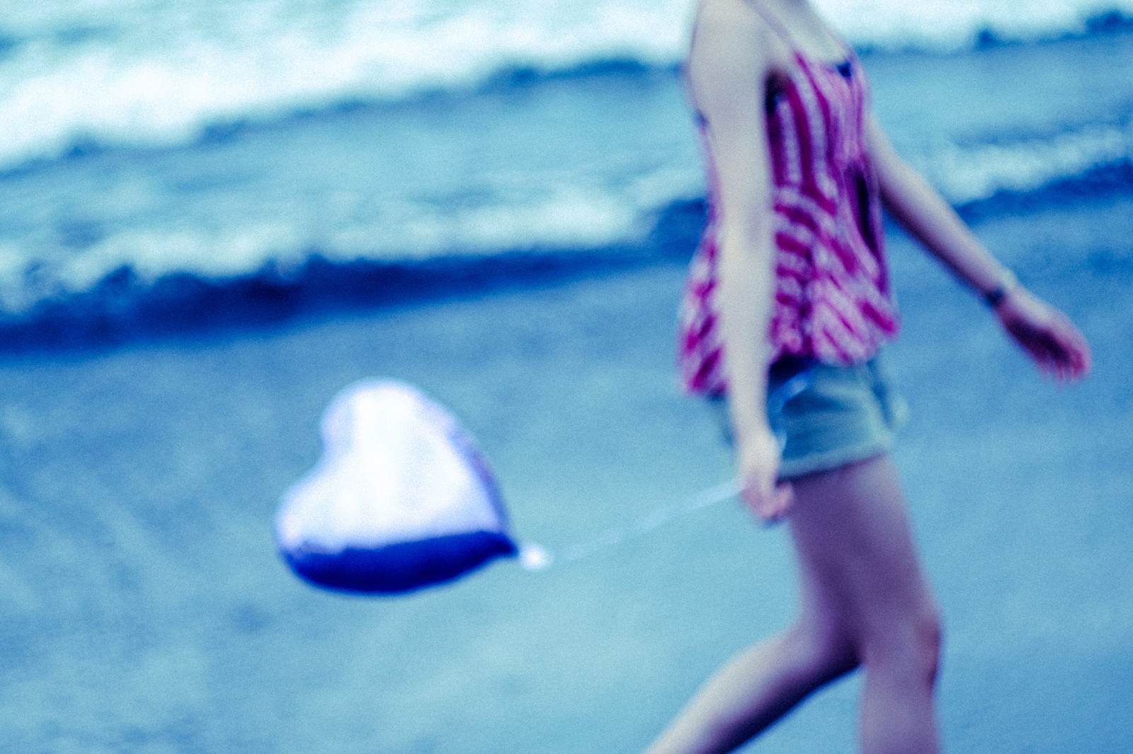 青い海を背景に白いハートを手に持って砂浜を歩く女性