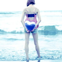 波打ち際で両手でハートを作る女性の後ろ姿の写真