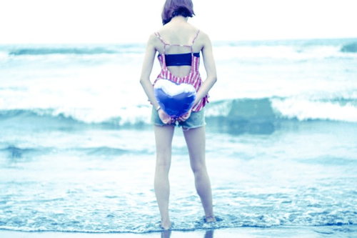 波打ち際で両手でハートを作る女性の後ろ姿