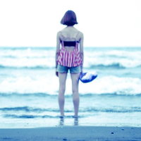 波打ち際で青い海を眺める女性の後姿、夏の砂浜で海を見つめるの写真