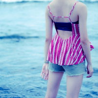 波打ち際に立ちすくむ若い女性の後ろ姿、ピンクストライプの水着姿で夏の海を眺めるの写真