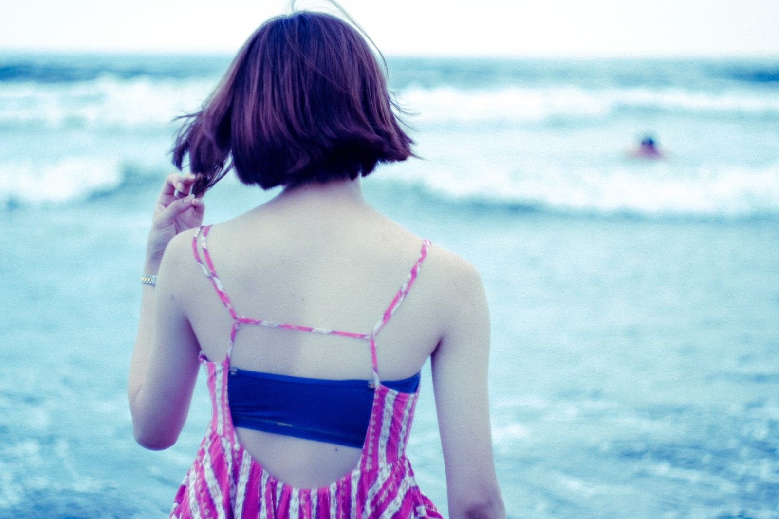 波打ち際にひとり立つ女性の後ろ姿