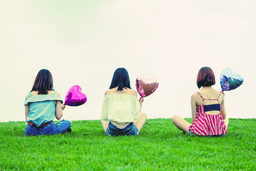 ハートの風船を持った女性3人の後姿、夏の芝生で友情を表現