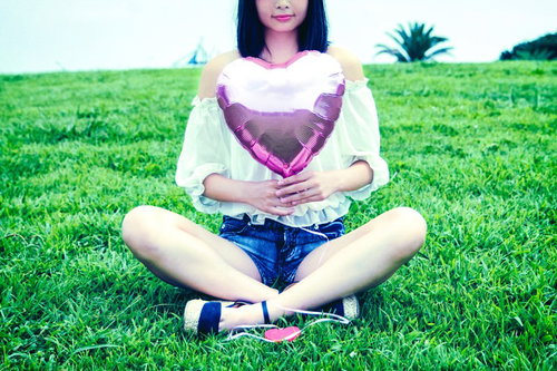 芝生に座るガーリー女子とピンクのハート型風船