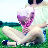 公園の芝生の上でハートの風船を持って座る女性の写真