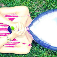 青いハート型の風船で顔を隠すピンクのボーダー服の女子の写真