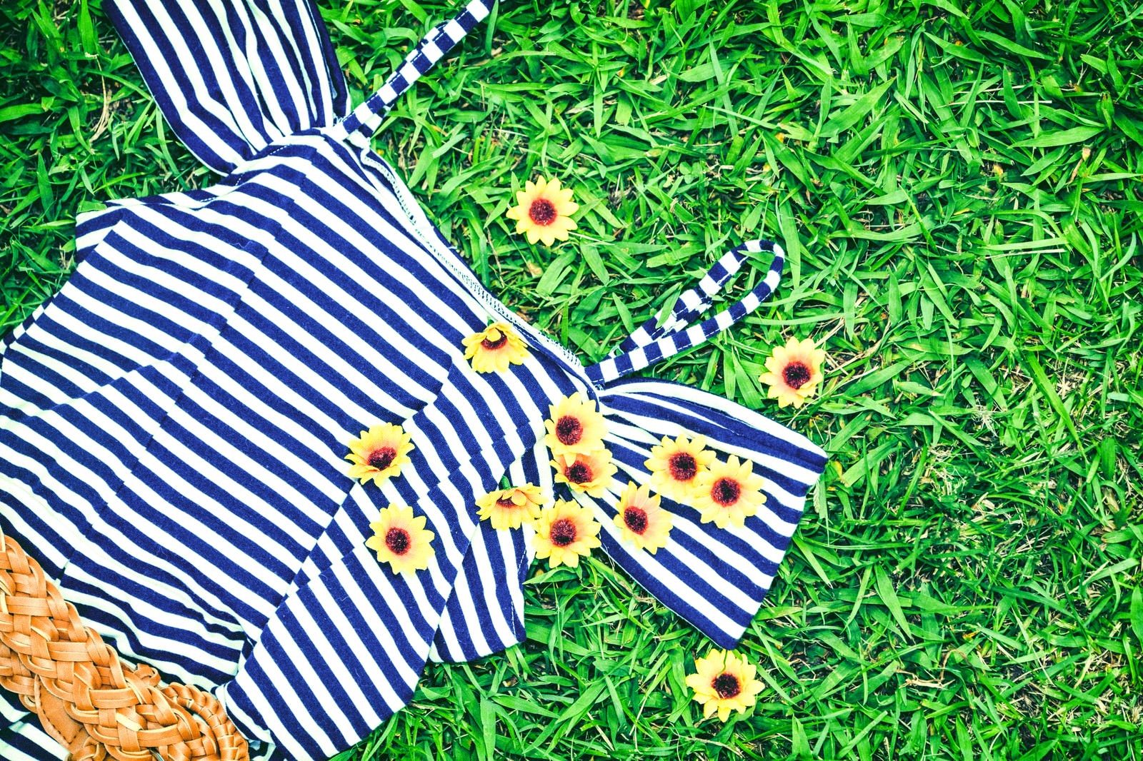 緑の芝生の上に置かれた青白ストライプの夏服と黄色い花のブローチ